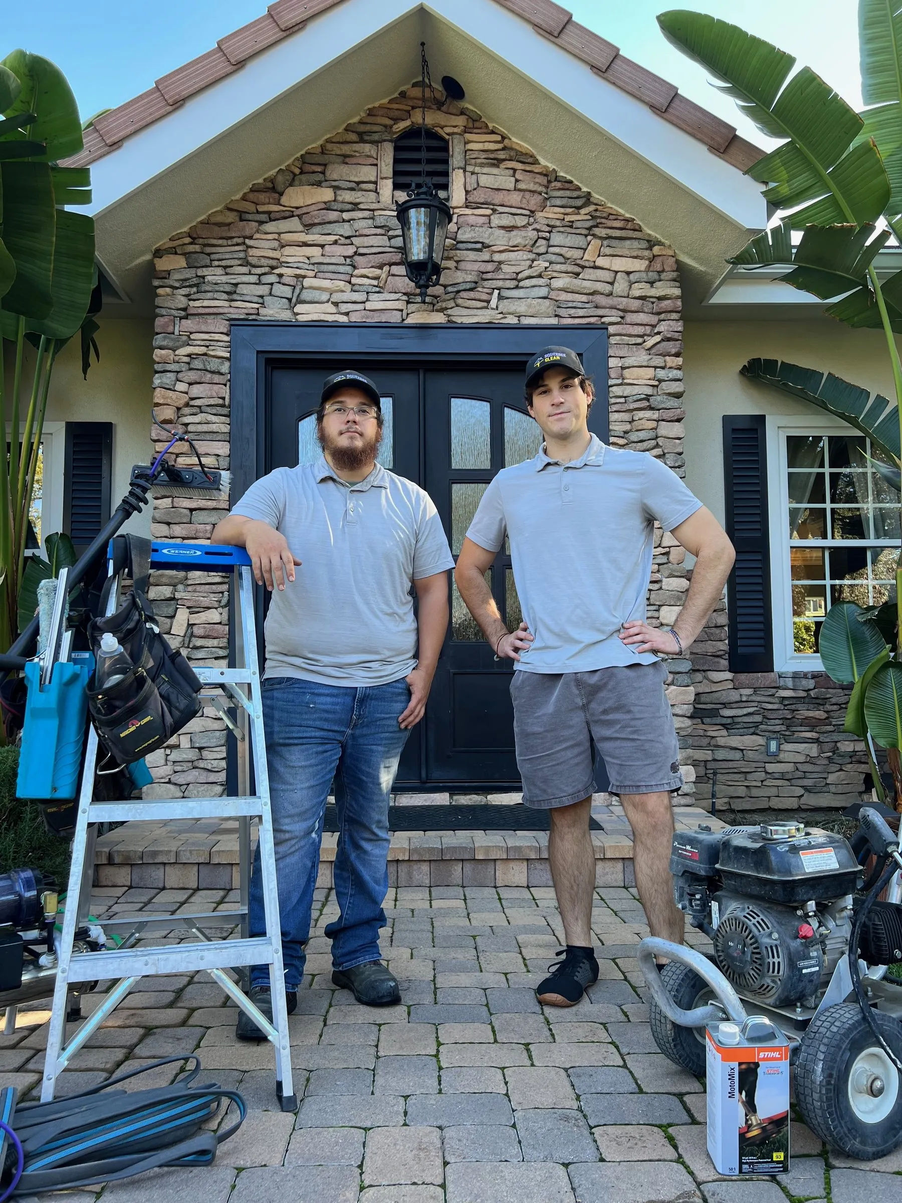 Two Squeegee Clean Windows crew members in uniform at a customer's front door with a ladder and pressure washer