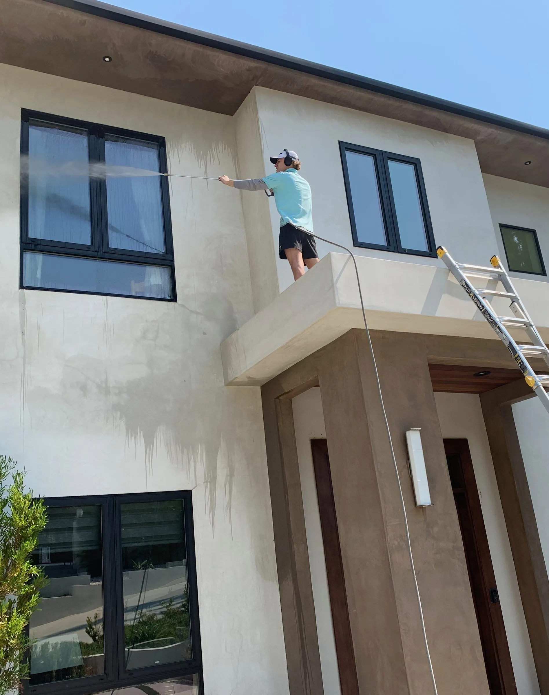 Technician on a balcony pressure washing a modern stucco facade