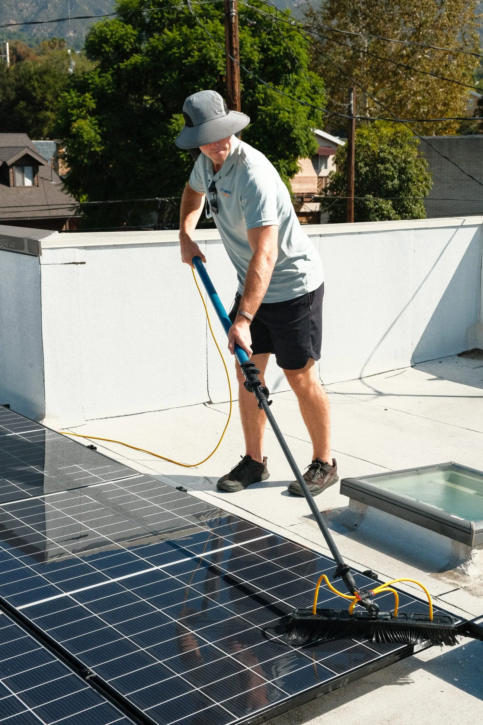 Elliot brushing rooftop solar panels with a water-fed pole, panels wet and reflecting the sky