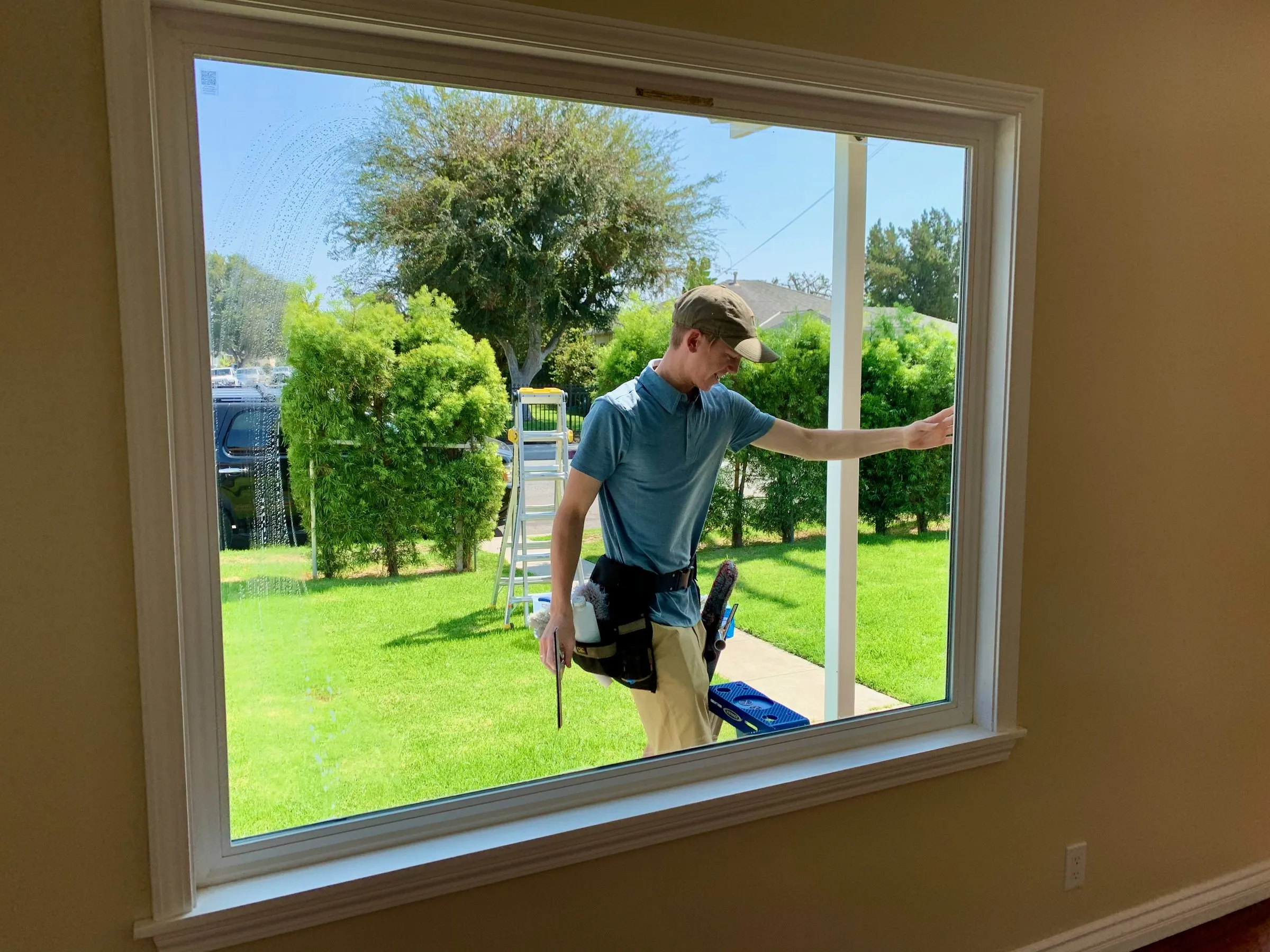 View from inside a home through a freshly cleaned picture window, technician outside, green lawn beyond